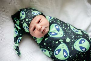 Cute newborn baby wrapped in black alien print swaddle blanket with matching knotted sleep cap.