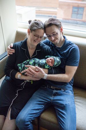 Happy new parents holding their newborn baby in alien print swaddle at hospital.