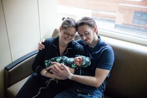 Smiling couple sitting together cradling their newborn baby wrapped in alien print blanket.