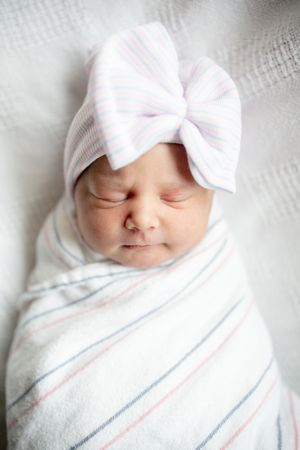 Sleeping newborn baby swaddled in striped hospital blanket wearing matching white bow hat.