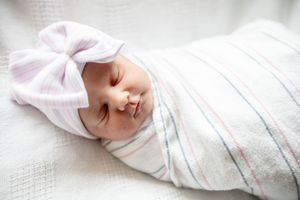 Peaceful newborn baby sleeping swaddled in striped blanket wearing white bow headband.