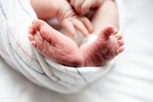 Close-up of newborn baby feet wrapped in a soft white swaddle blanket.