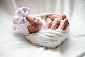 Newborn baby swaddled in striped blanket with bow hat, tiny feet peeking out.