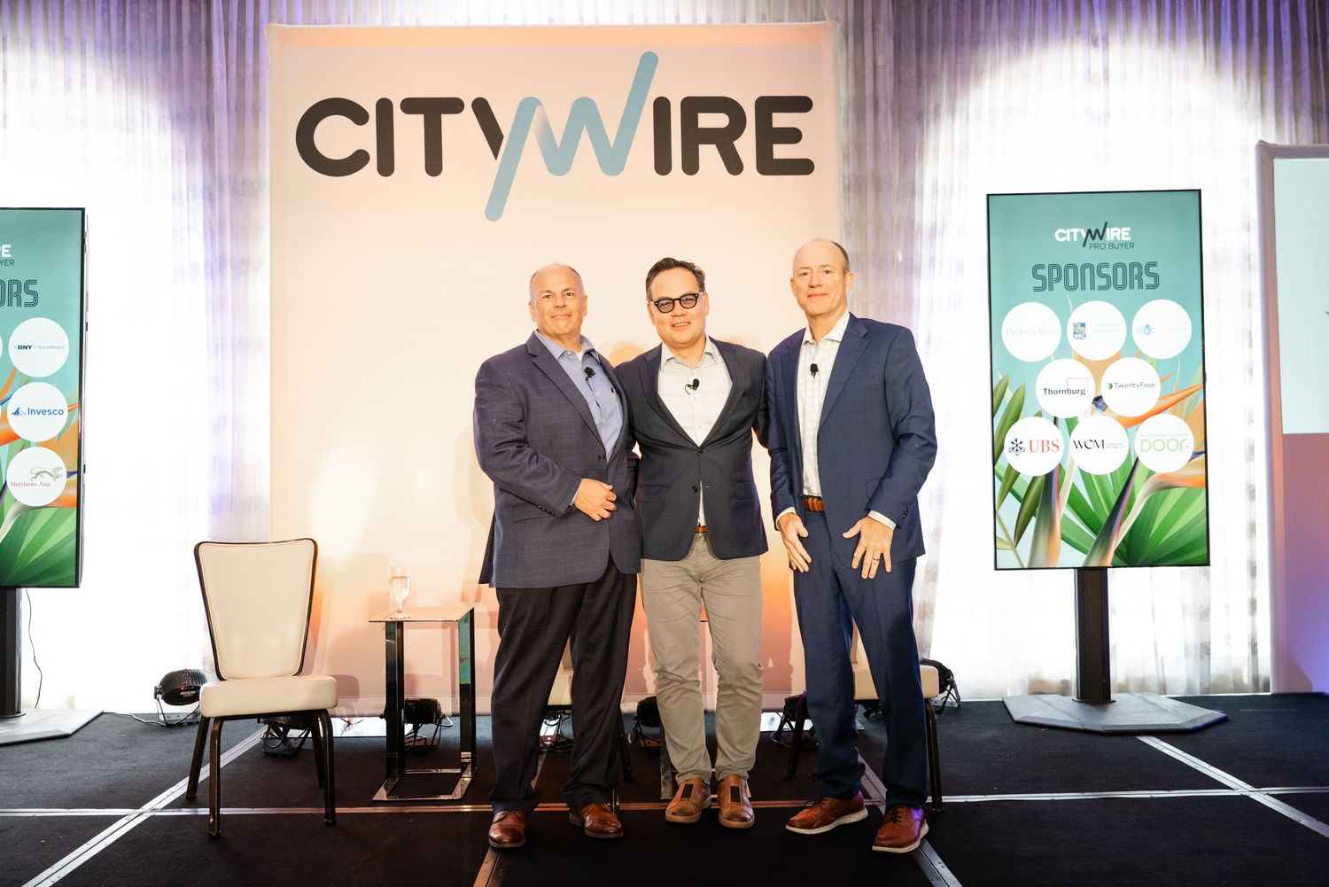 Three professionals pose together on stage at a Citywire financial conference event.