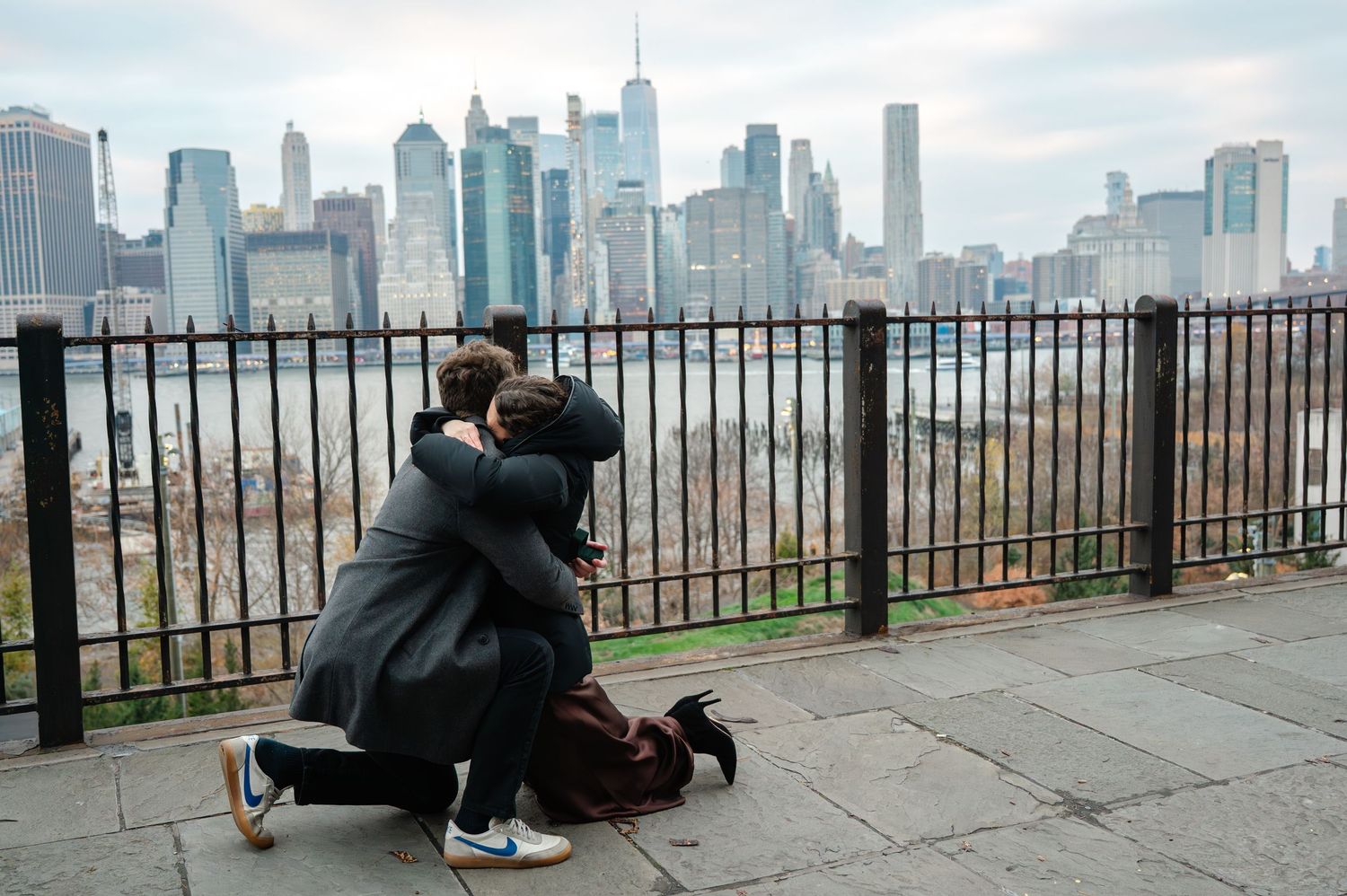 Couple sharing a romantic marriage proposal moment on one knee with NYC skyline backdrop.
