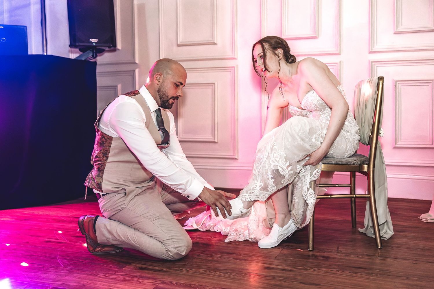 Candid wedding moment groom helps bride with her shoes on dance floor.