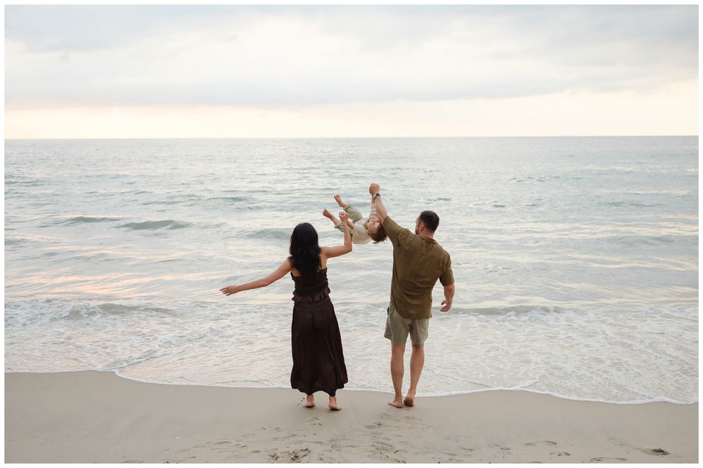 Family photo session in Puerto Vallarta with parents swinging baby at sunset on the beach.