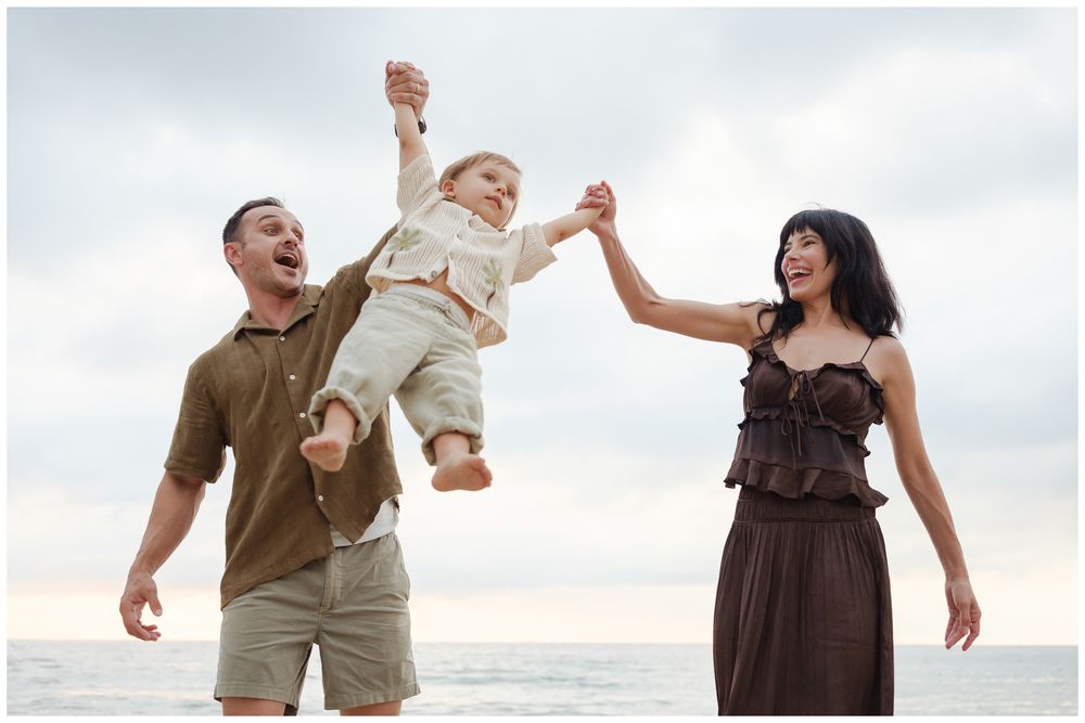 Family photo session in Puerto Vallarta with parents lifting toddler on a cloudy beach day.