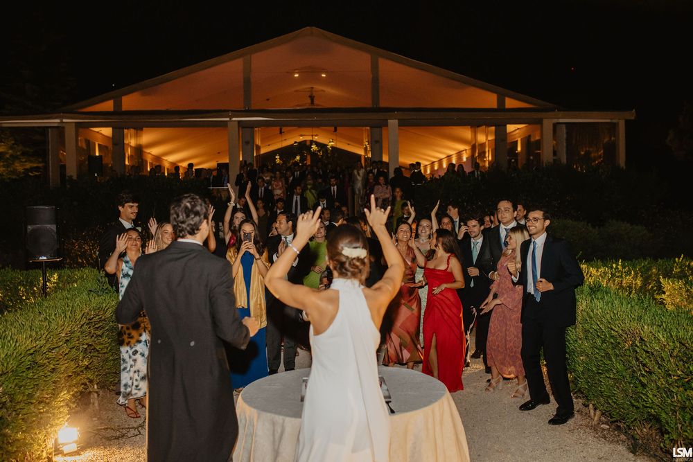 Bride and groom celebrate with guests outside an elegant lit venue during evening wedding reception.