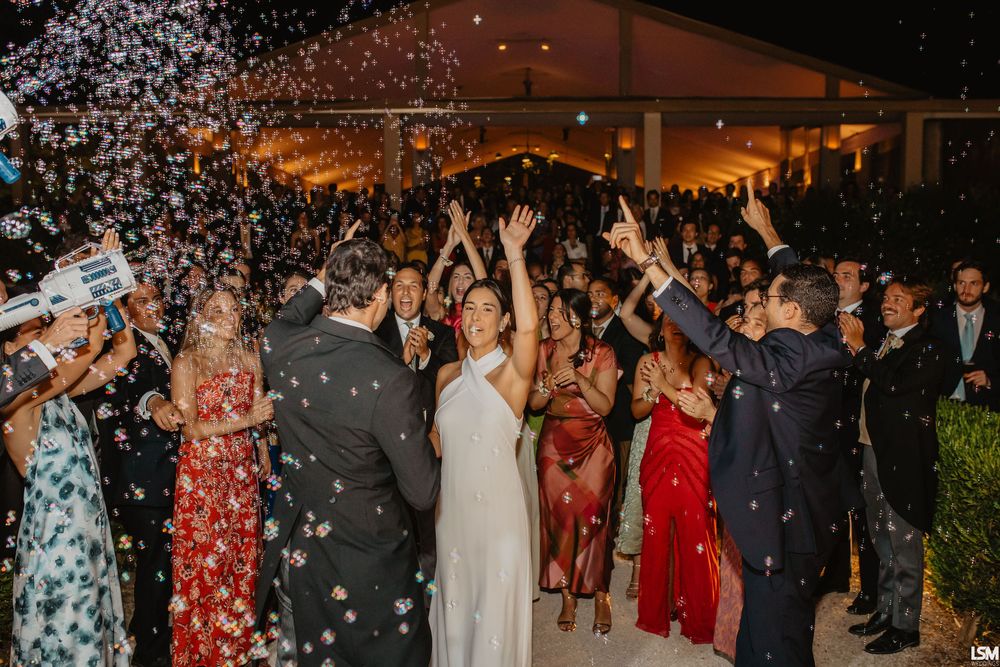 Bride and groom celebrated with confetti shower by guests at outdoor evening wedding reception.
