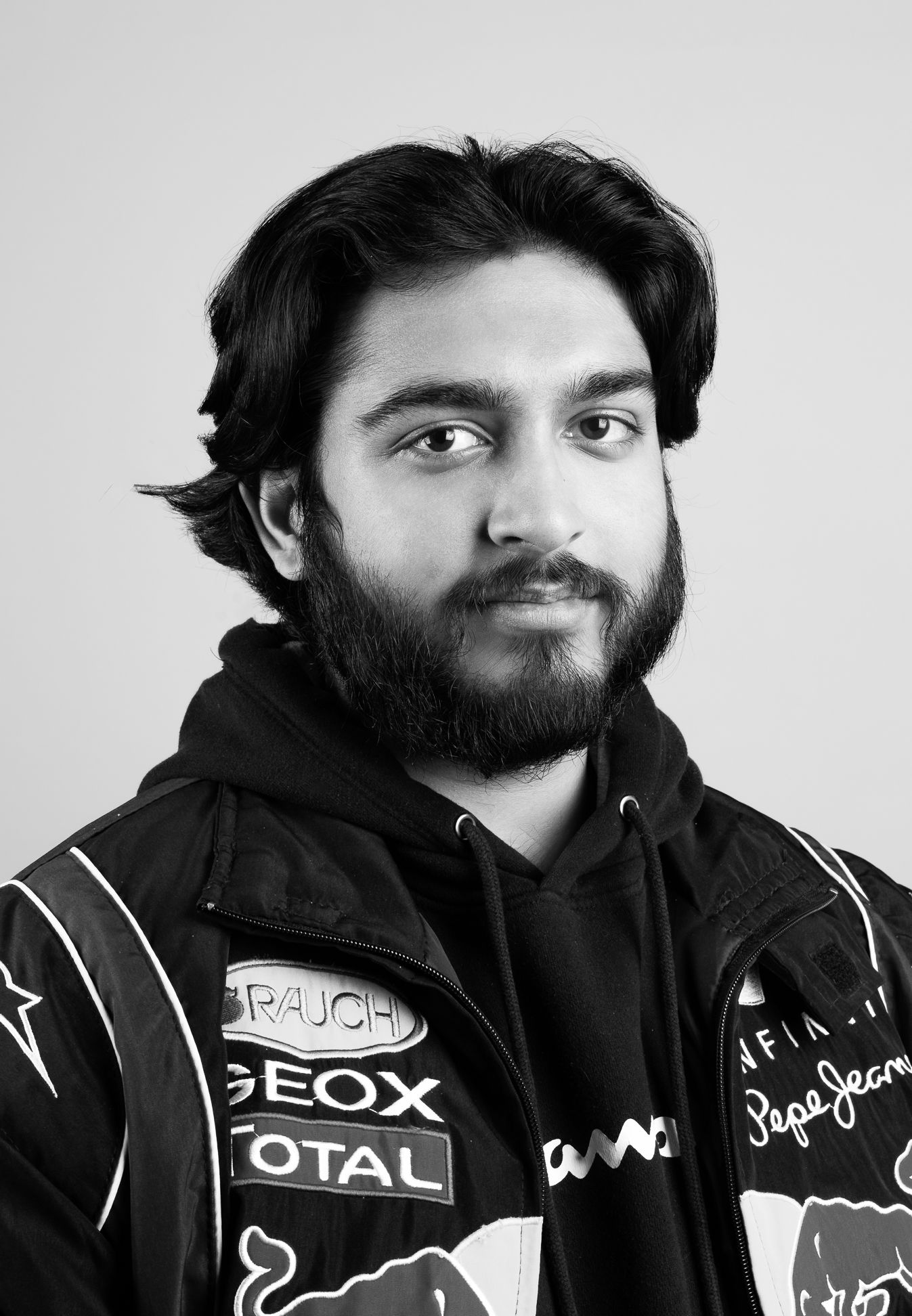 Black and white image of a man in a racing jacket and hoodie, smiling and looking at the camera