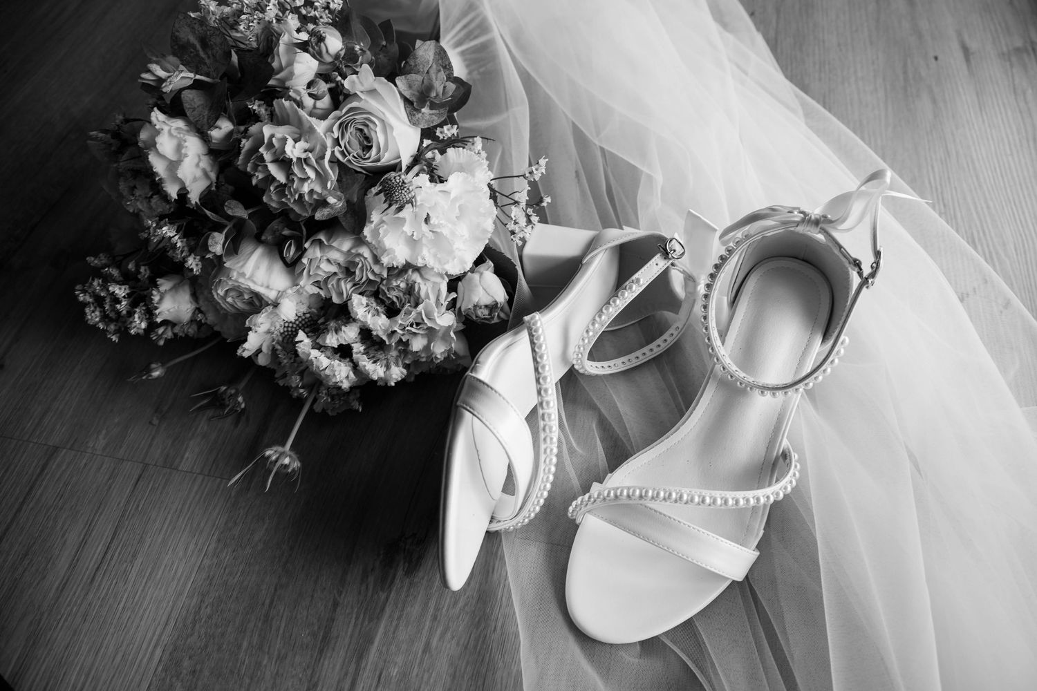 Black and white photo of elegant wedding accessories featuring satin ribbon bows, bridal garter, and floral bouquet.