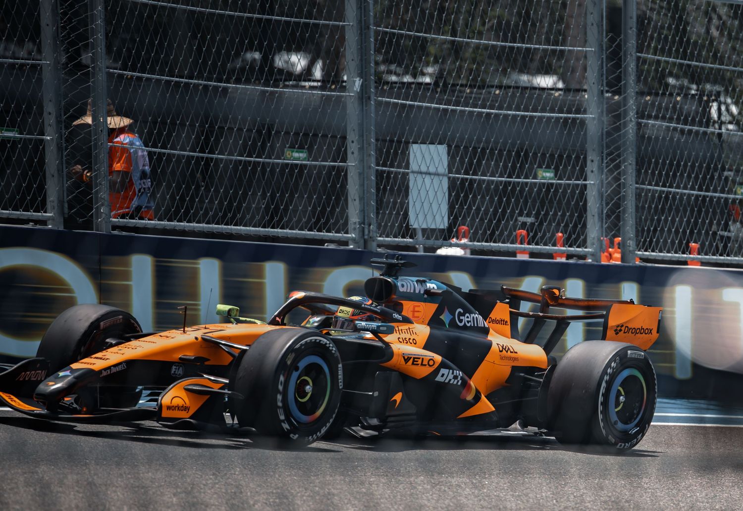 Two McLaren F1 cars in orange livery racing closely together on a street circuit during a Formula 1 Grand Prix.