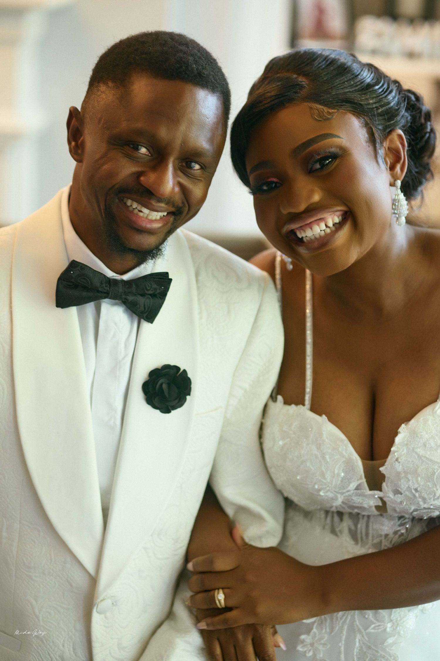 Smiling bride and groom in white wedding attire posing together on their wedding day.