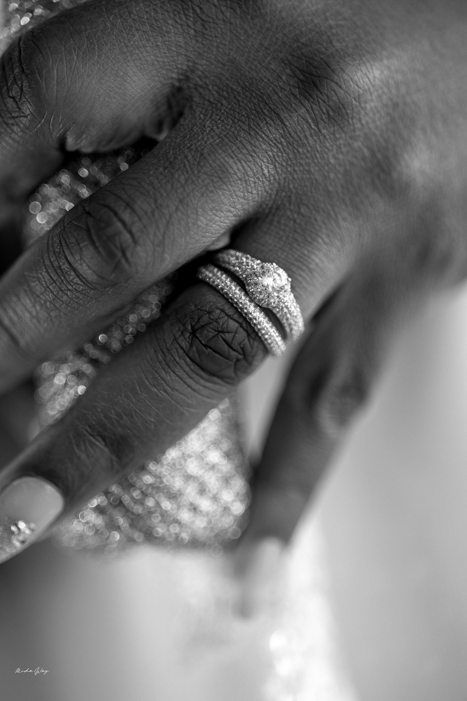 Close-up black and white photo of hands wearing elegant diamond wedding rings during a wedding ceremony.