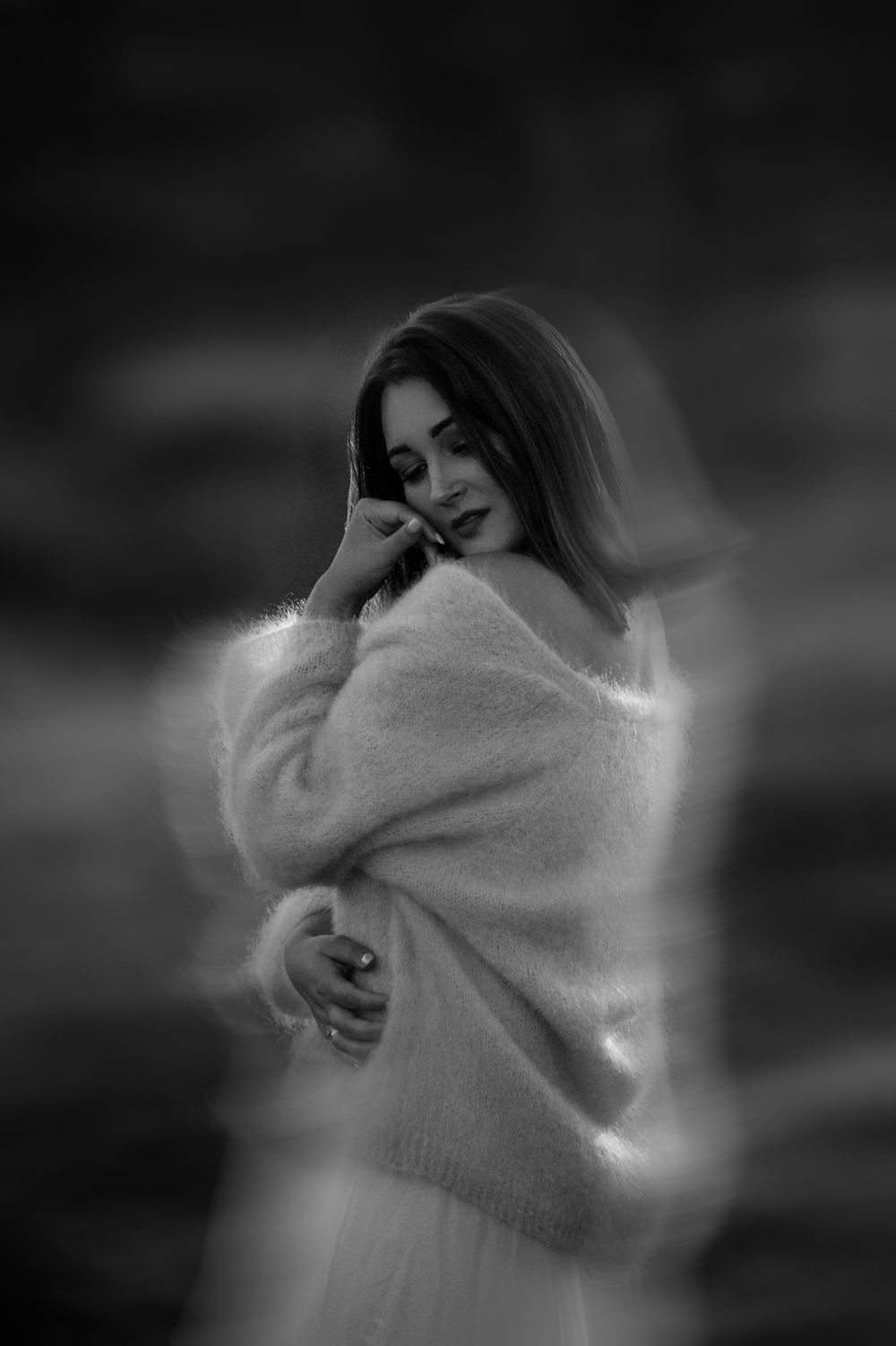 Black and white portrait of a young woman in a fluffy oversized sweater, posing dreamily with a blurred bokeh background.