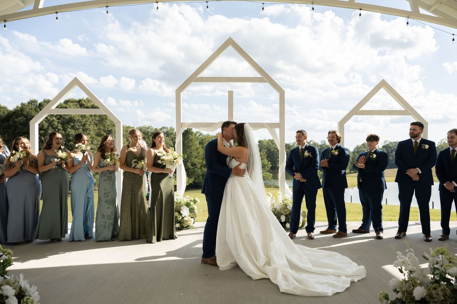 Bride and groom share a romantic dip kiss on a waterfront pier with a historic lighthouse in the background.