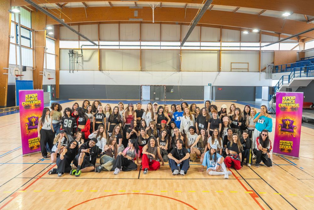 Large group of diverse young women posing together in a gymnasium at a dance or sports event.