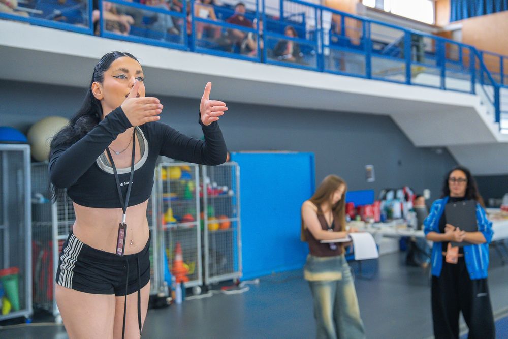 Female dancer performing choreography in gym while people watch in background.