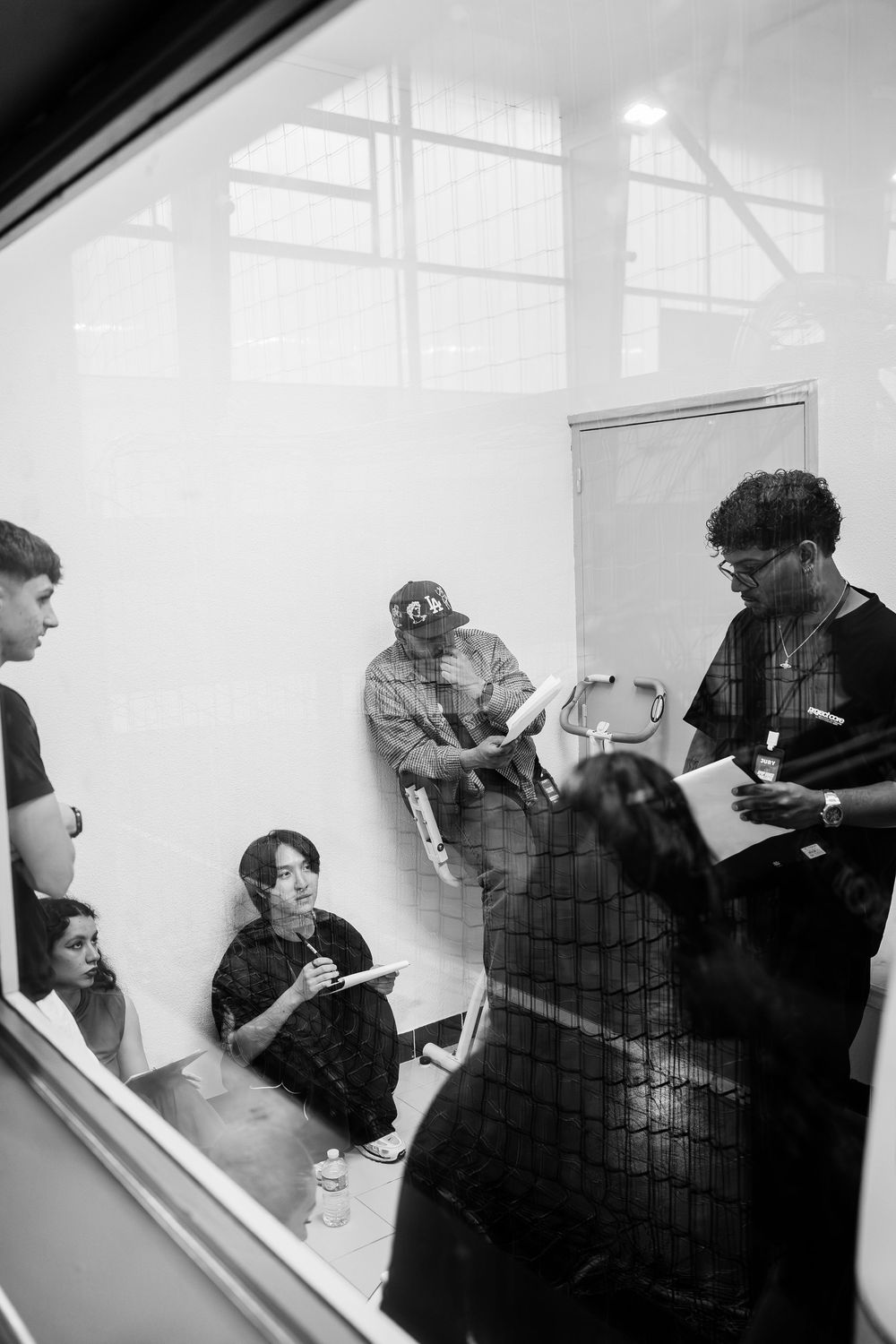 Black and white photo of a diverse group of people in a bright room, some seated, reviewing documents together.