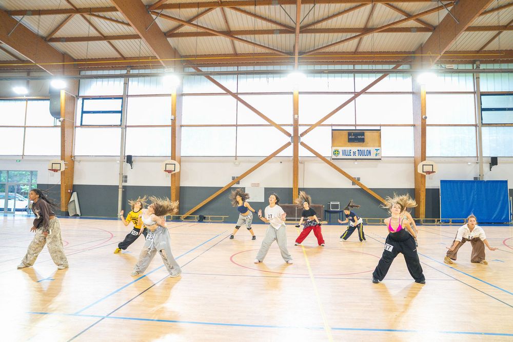 Group of people practicing dance or martial arts in a large indoor sports gymnasium with wooden floors.