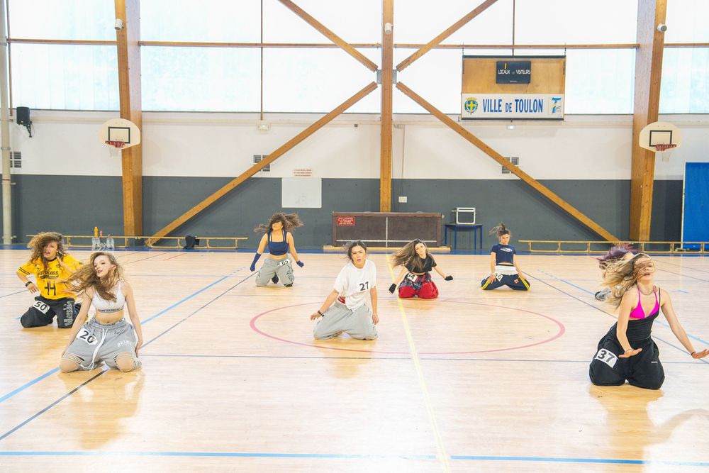 Girls practicing dance choreography on a gymnasium floor in Toulon, France, kneeling in formation.