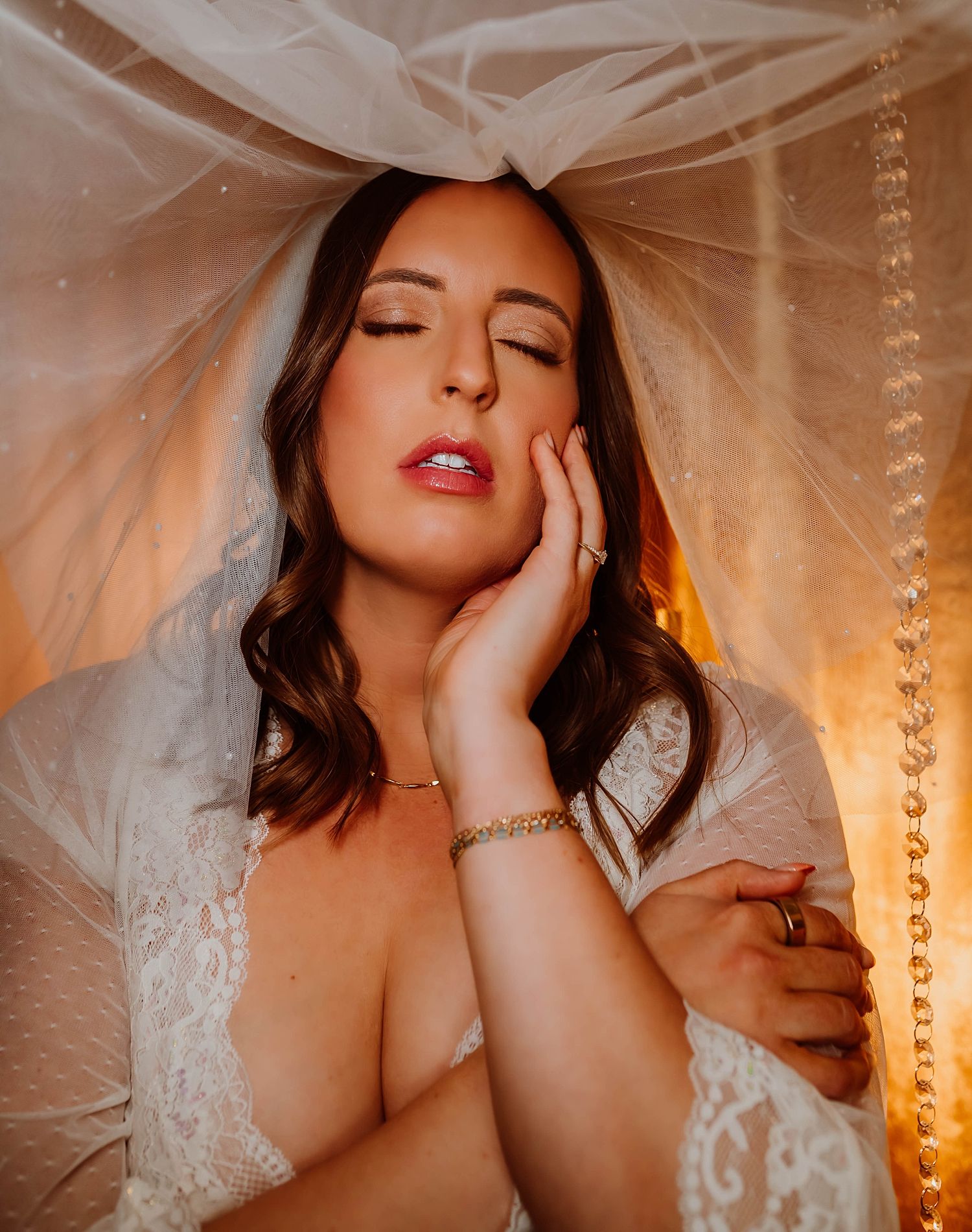 A bride in white lace poses dreamily under a sheer veil answering what you need to know about boudoir