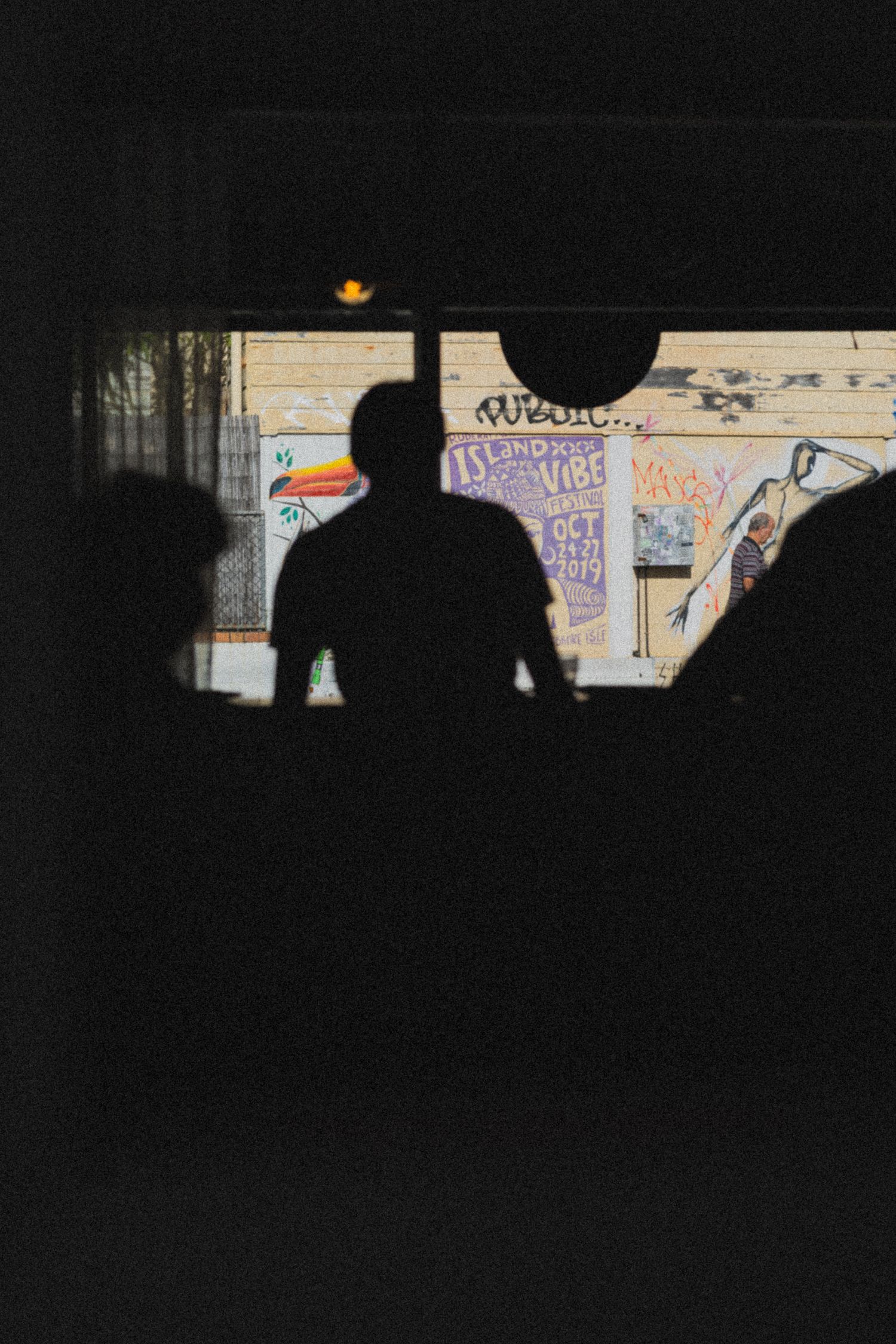 Silhouettes of people standing in front of a graffiti-covered brick wall with colorful posters and warm lighting.