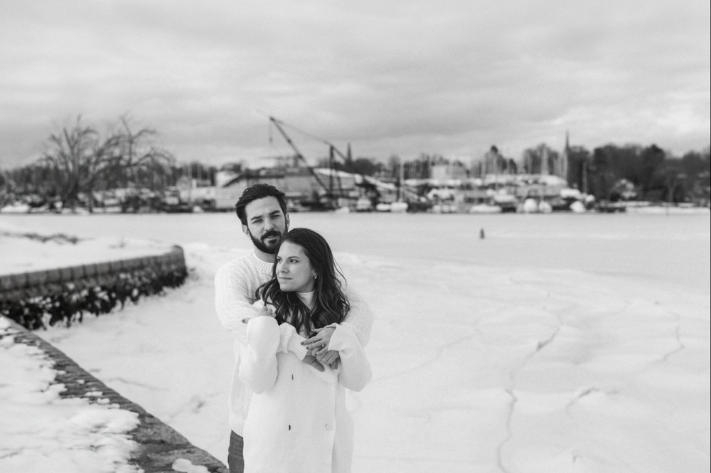 Couple embracing in snowy winter landscape, black and white engagement photo outdoors.