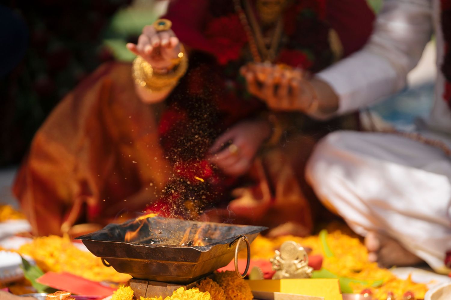 Hindu wedding ceremony with sacred fire ritual, flower offerings, and traditional attire during a colorful religious puja.