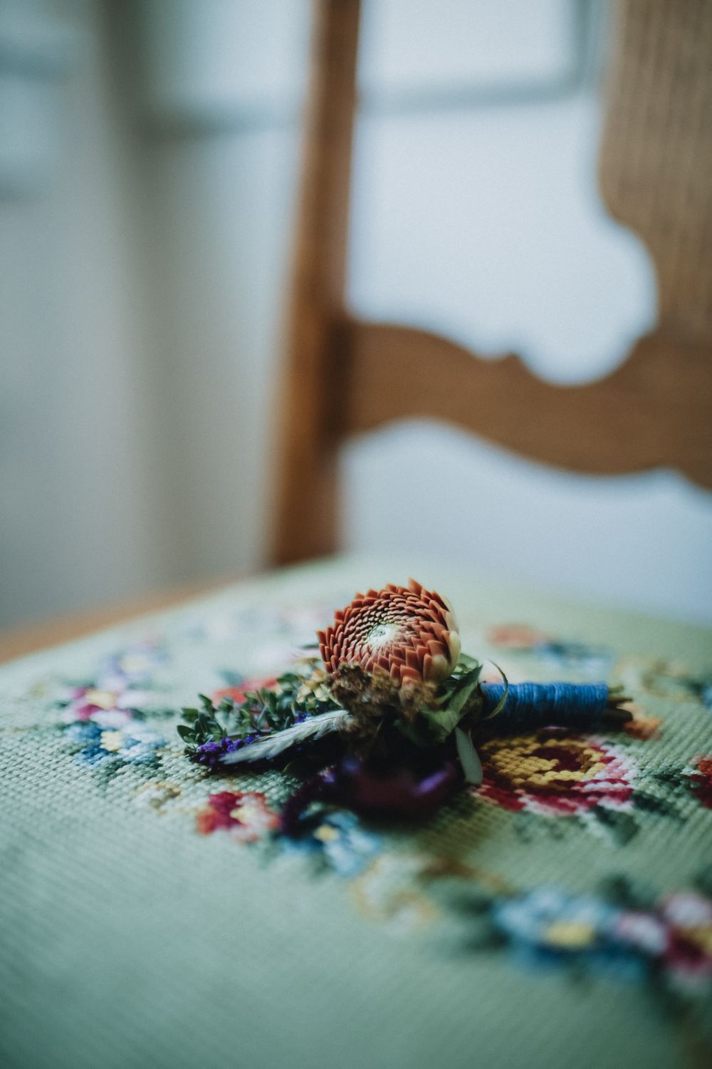 A boutonniere with a dried protea flower rests on a n antique floral needlepoint chair seat. Kennebunkport York wedding photographer.