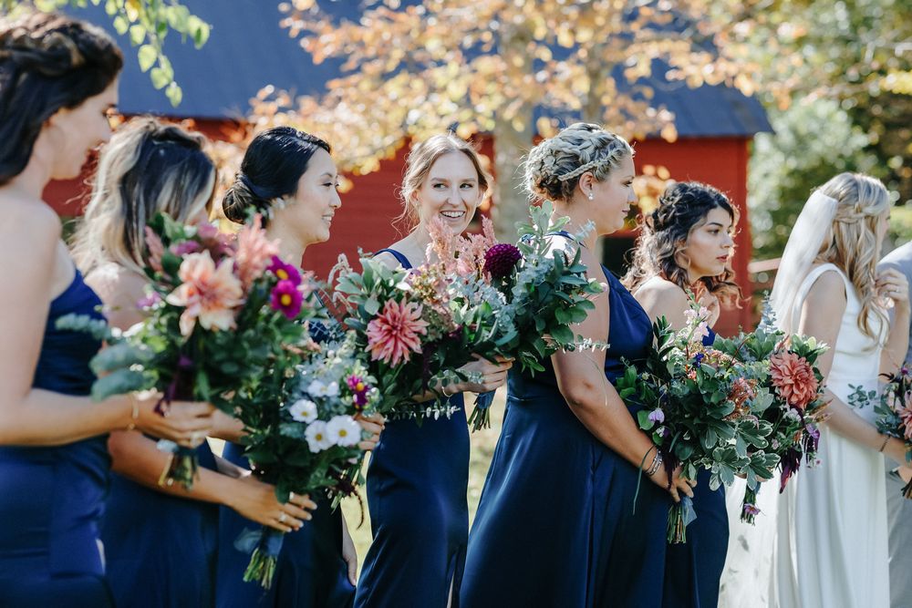 Bridesmaids in navy blue dresses holds flowers smiling with autumn foliage. North Shore wedding photographer.