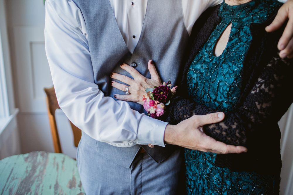 Mother of the groom and groom in gray vest embraces her wearing a floral corsage for getting ready photos. Laconia wedding photographer.