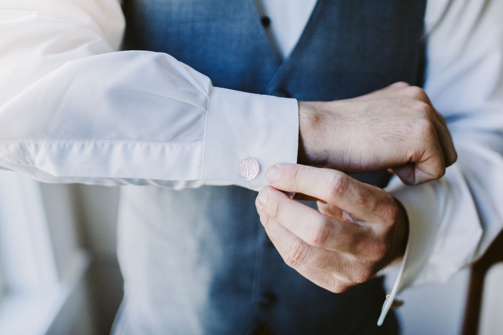 Man in white dress shirt and blue vest fastens cufflink on sleeve during getting ready photos. Monadnock Southern NH wedding photographer