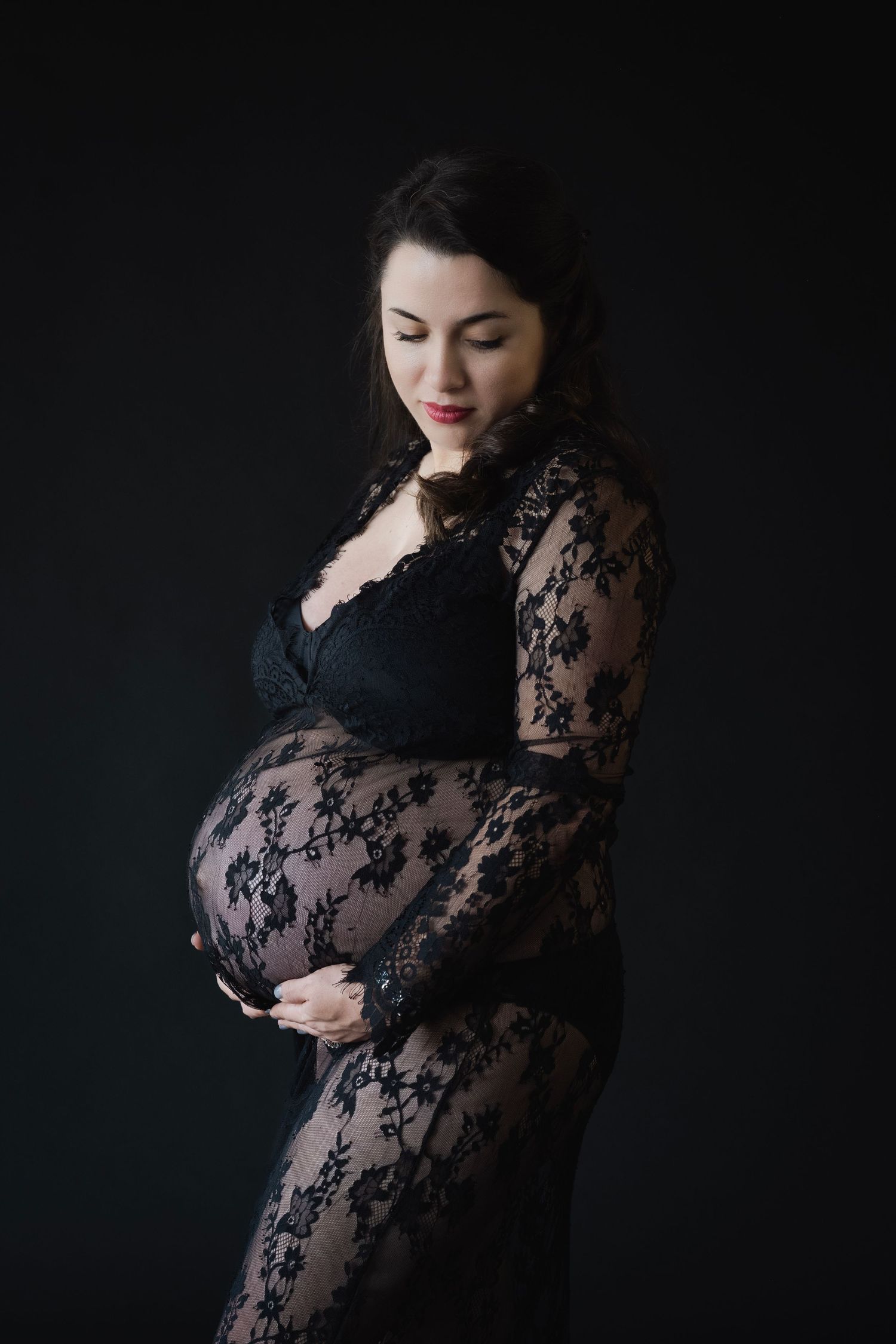 Artistic maternity portrait in black lace against dark background.
