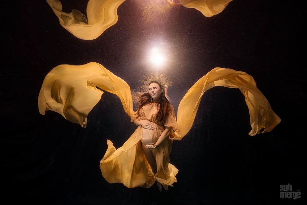 Billowing yellow fabric creates abstract shapes around a bright light source in a dark studio setting.