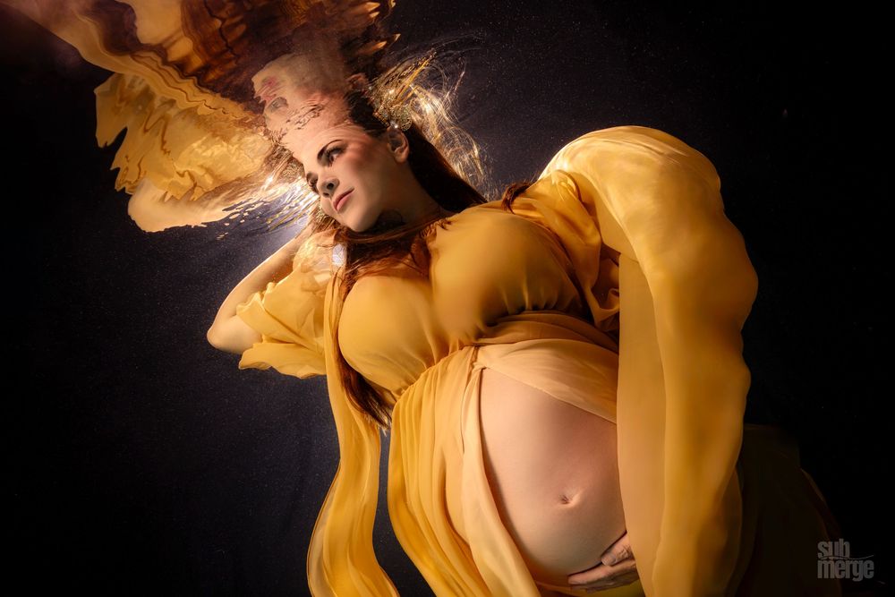 A figure in flowing yellow fabric creates ethereal movement against a dark background.
