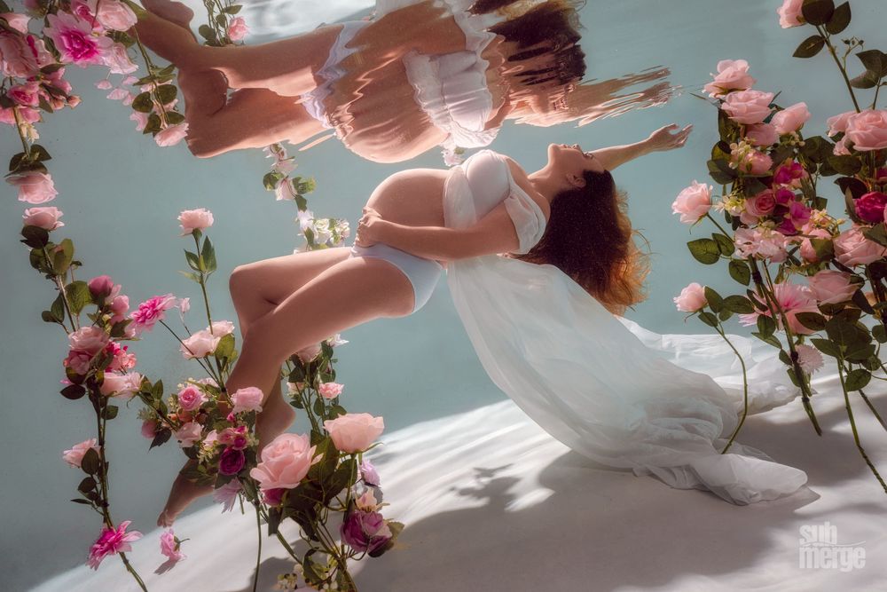 Underwater portrait with pink roses framing a flowing white dress in ethereal light.