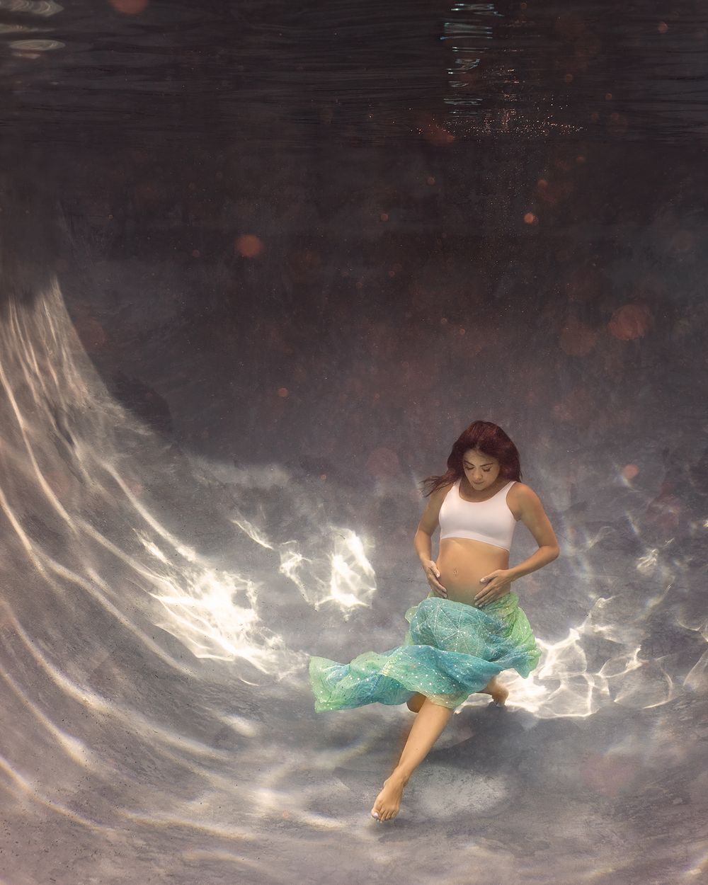 Ethereal underwater photography with flowing teal fabric creating dramatic movement against dark background.