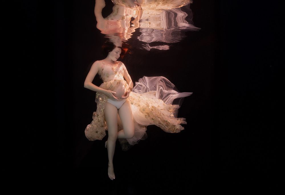 Dramatic underwater dance photography with flowing fabric creating ethereal movement against black background.