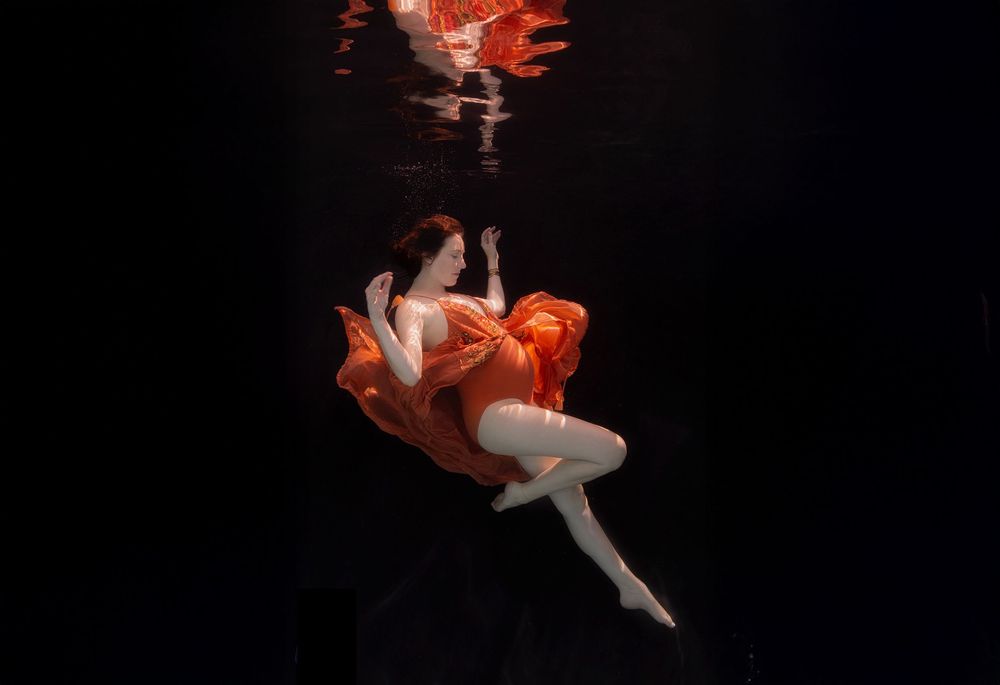 A sequence of orange and white goldfish swimming gracefully against a black background in an artistic composition.