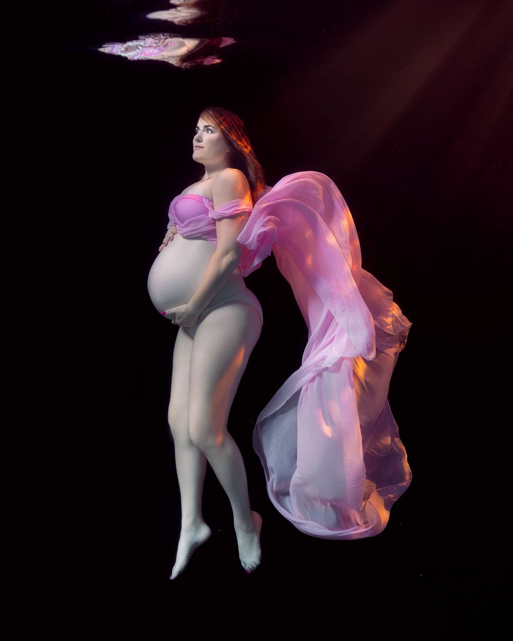 Underwater photo of a figure in a flowing pink dress floating gracefully against a dark background.