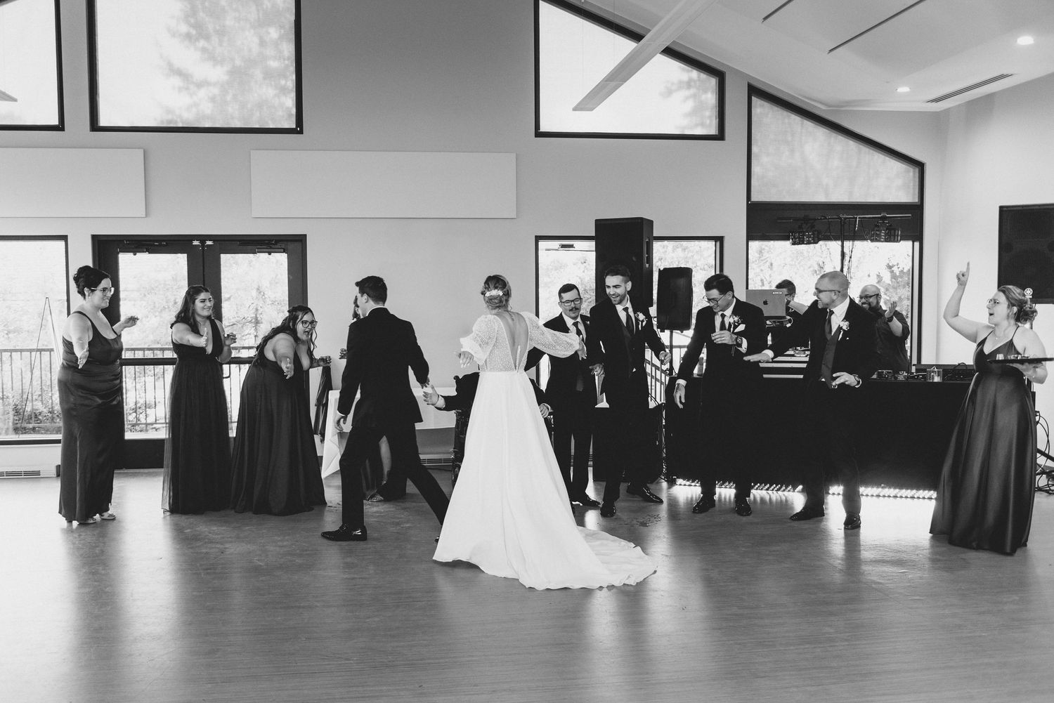 Black and white photo of wedding guests mingling at a reception while a couple dances on the dance floor.