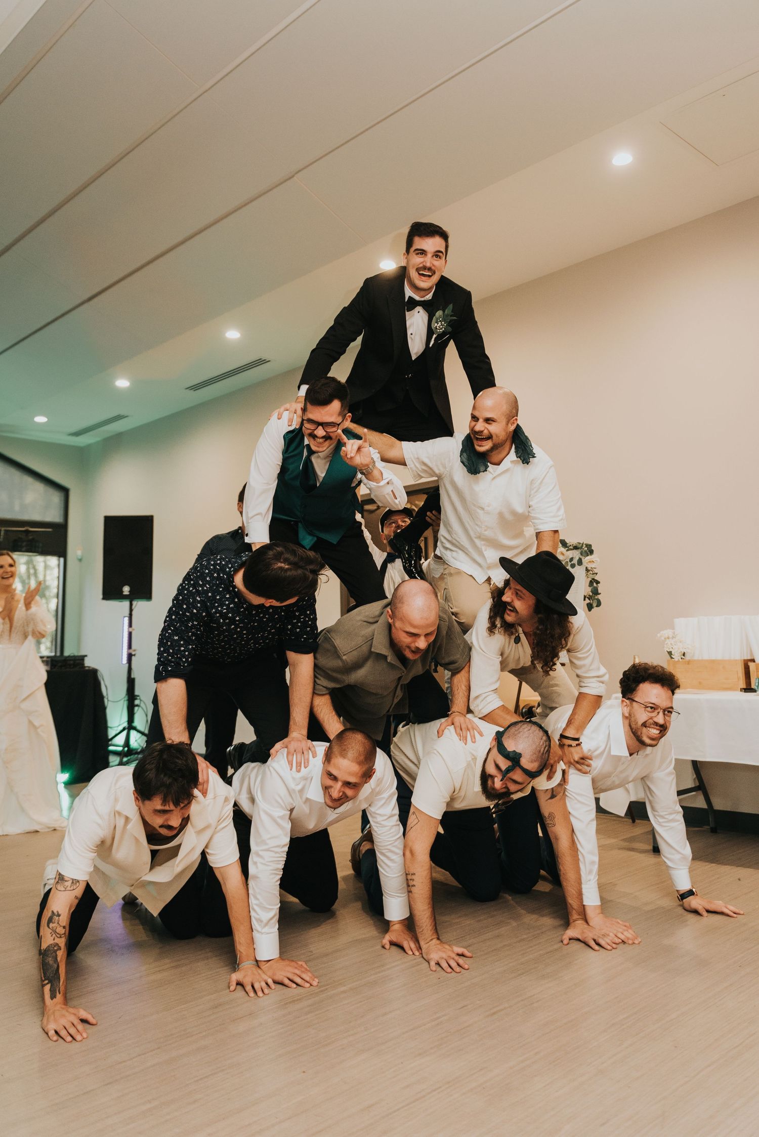 A group of wedding guests performing a synchronized crawling formation indoors.