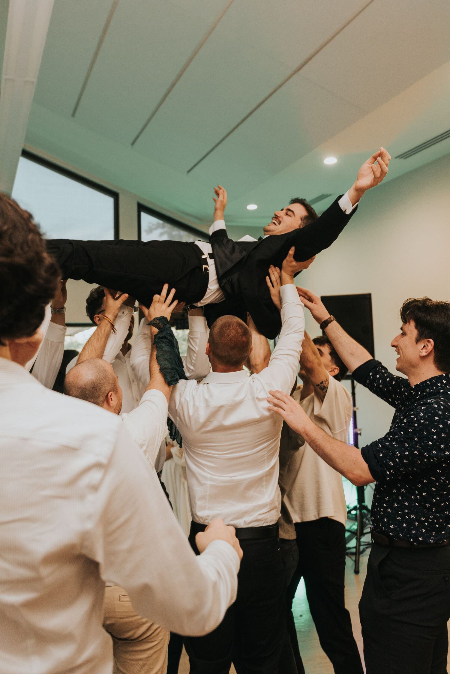 A group of people dancing with their arms raised in celebration at an indoor event.