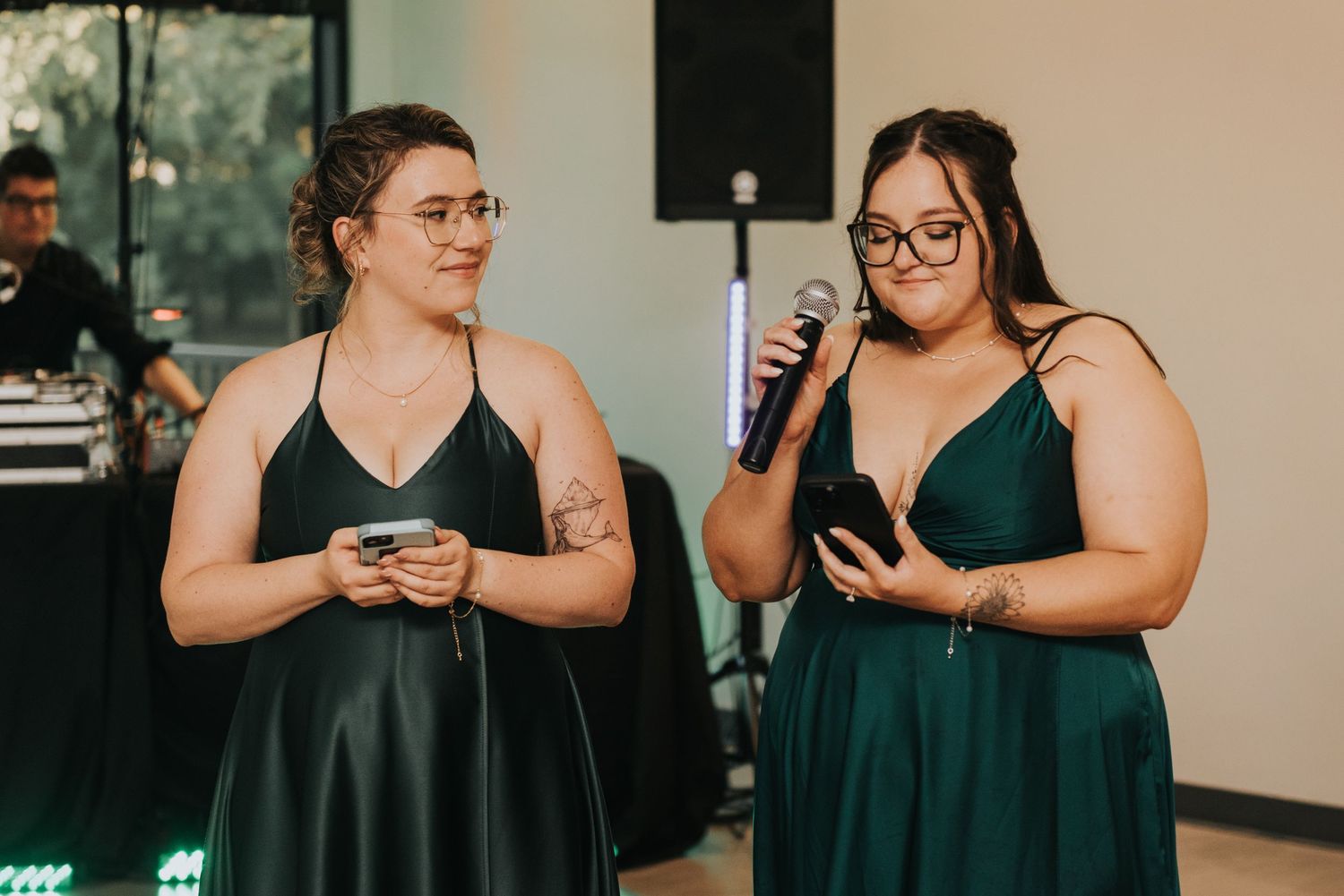 Two women in emerald green formal dresses stand together holding microphones at an event.
