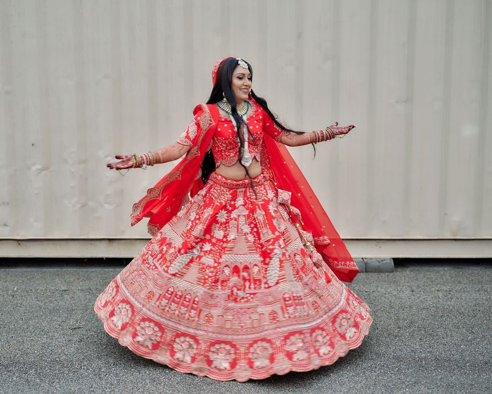 Bride in red lehenga twirling to show off the intricate embroidery details against grey background.