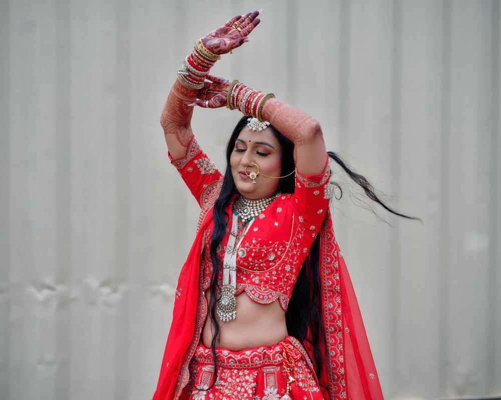 Traditional Indian bride in vibrant red attire poses gracefully during wedding ceremony preparations.