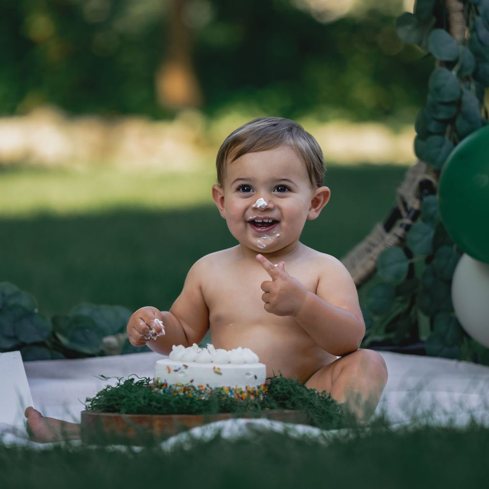 Baby smiling with cake on face during first birthday cake smash outdoors.