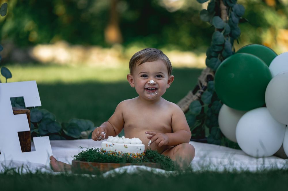 Happy baby smiling during outdoor cake smash with green and white balloon decor.